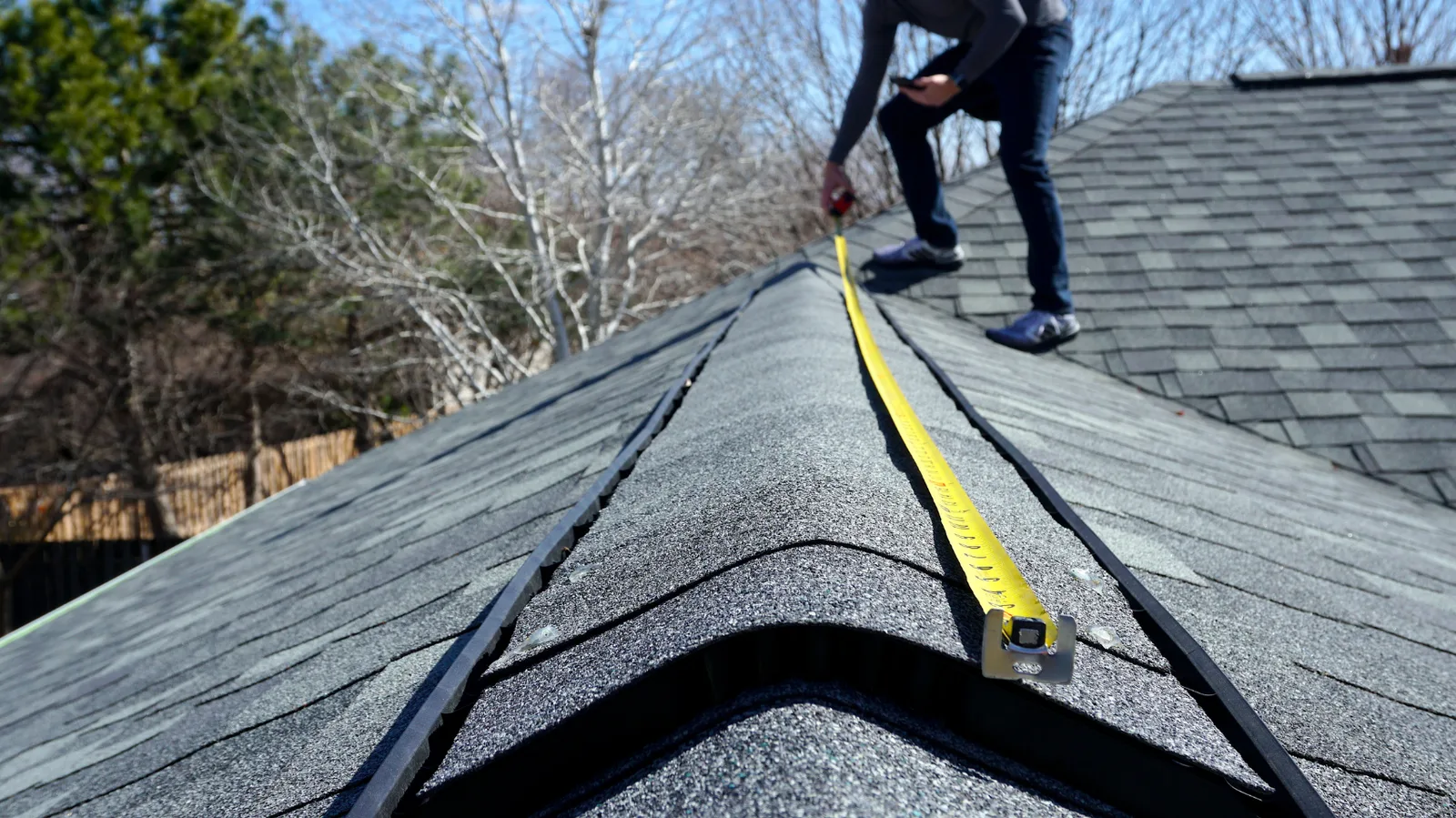 A roofer measuring along a shingle ridge with a tape measure