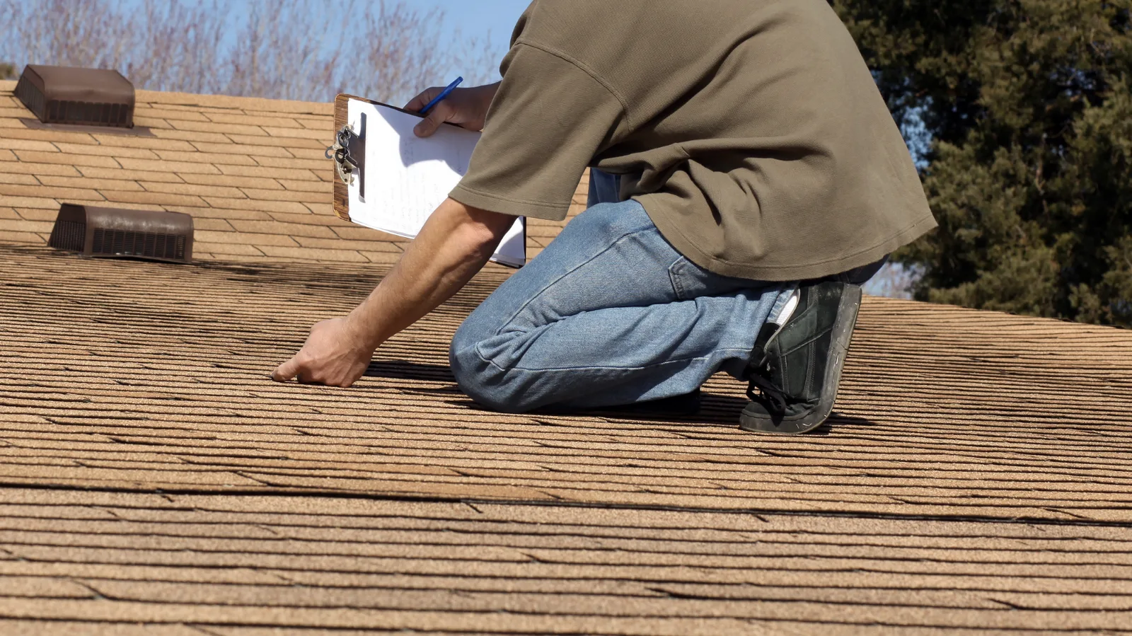 An inspector with a clipboard checking shingles near roof vents